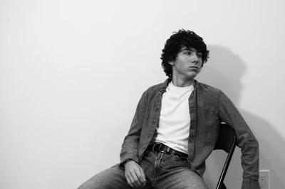 Monochrome photo of Nicholas Fortune sitting in a folding chair staring off into the distance glamorously