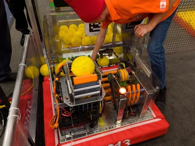 A photo of FRC Team 2013's 2026 season robot stopped on a game field with a person inspecting it